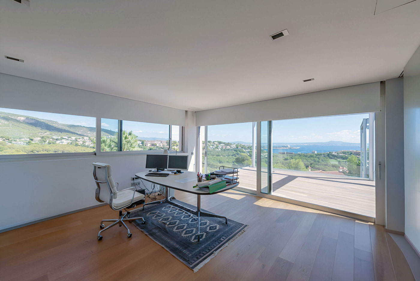 Arbeitszimmer mit modernem Schreibtisch, Holzfußboden und Glasfront mit Blick auf die Küste von Mallorca