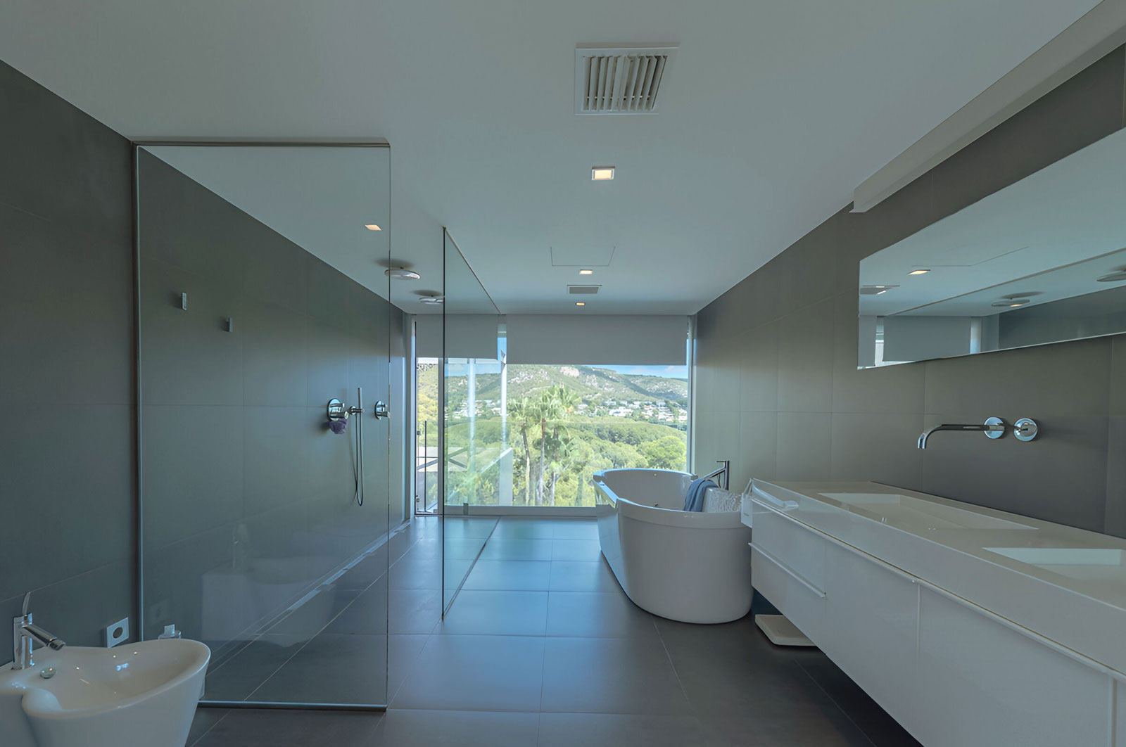 Luxuriöses Badezimmer mit freistehender Badewanne, bodentiefer Dusche und Panoramafenster mit Naturblick