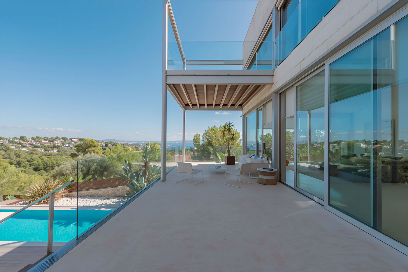 Großzügige Terrasse einer modernen Villa auf Mallorca mit Glasgeländer, Lounge-Möbeln und Blick über den Pool bis zum Meer