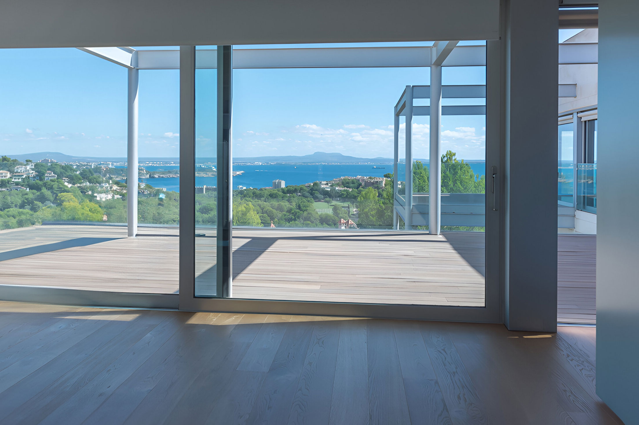 Innenraum mit hellem Holzfußboden und großflächiger Schiebetür zur Terrasse mit Meerblick und grünem Panorama